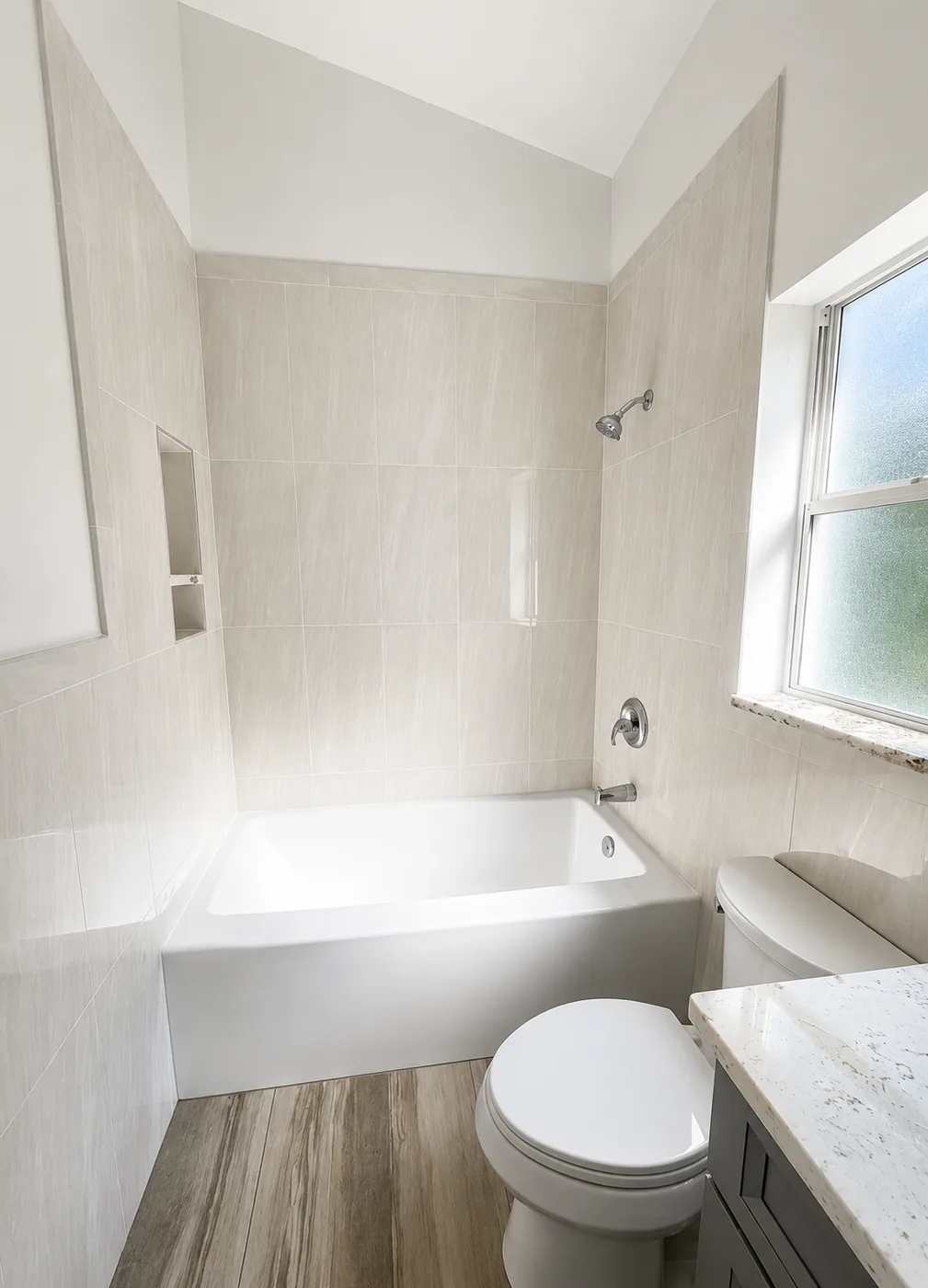 Bathroom remodel replacing dated beige wall tile with large-format porcelain tile, a new soaking tub, tiled niche and wood-look vinyl plank flooring - After