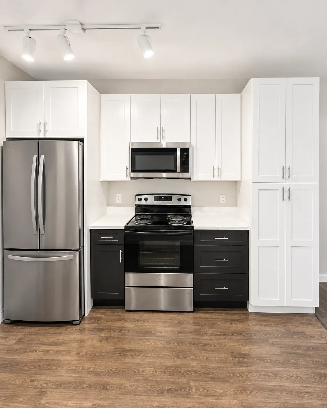 Kitchen remodel replacing honey oak cabinets with two-tone white and black shaker cabinetry, quartz countertops and wood-look vinyl plank flooring - After